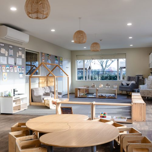 Warm preschool learning environment with Montessori furniture, low shelves and calm play spaces for early childhood education.